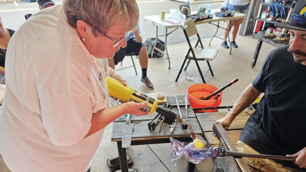 Participant enjoying a hands-on glassblowing session with professional guidance in a studio setting.
