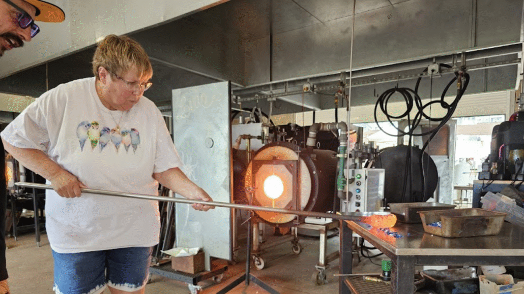 Woman enjoying a hands-on glassblowing session while shaping molten glass in a professional studio